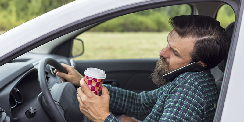 man drinking coffee and on phone whilst driving