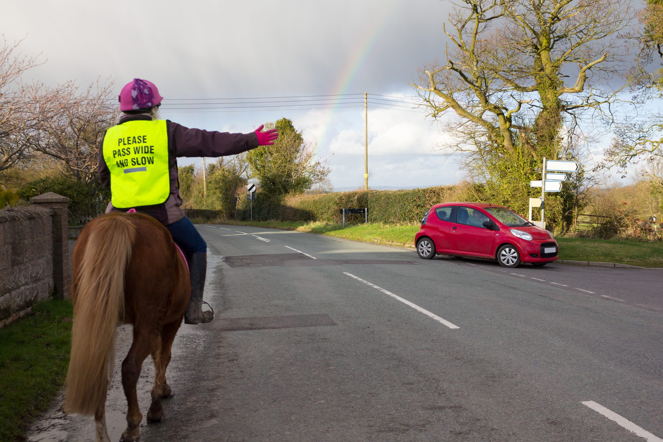 horse rider about to turn right on a road as a car drivers down the road