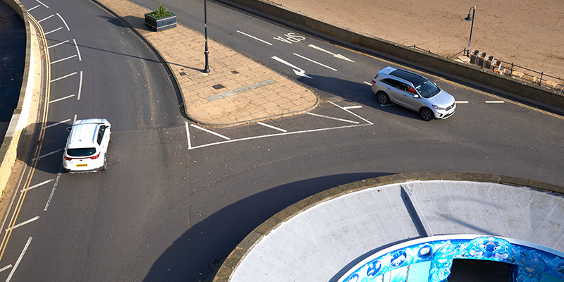 Two cars driving across a large roundabout