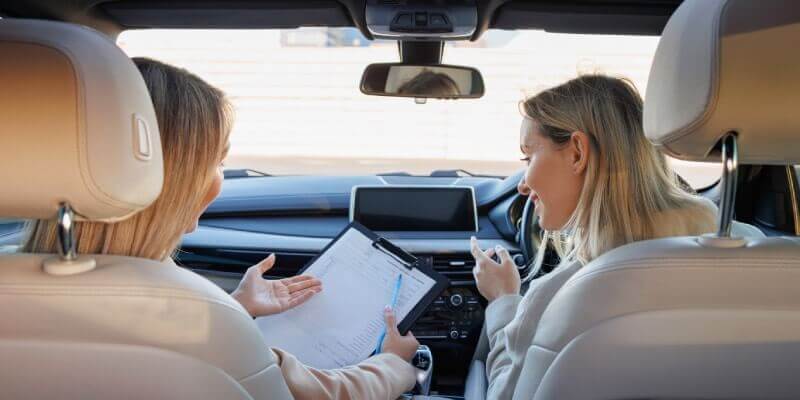 Examiner and learner discussing and looking at test marking sheet in car