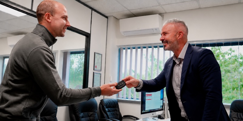 Two men exchanging a car key and smiling