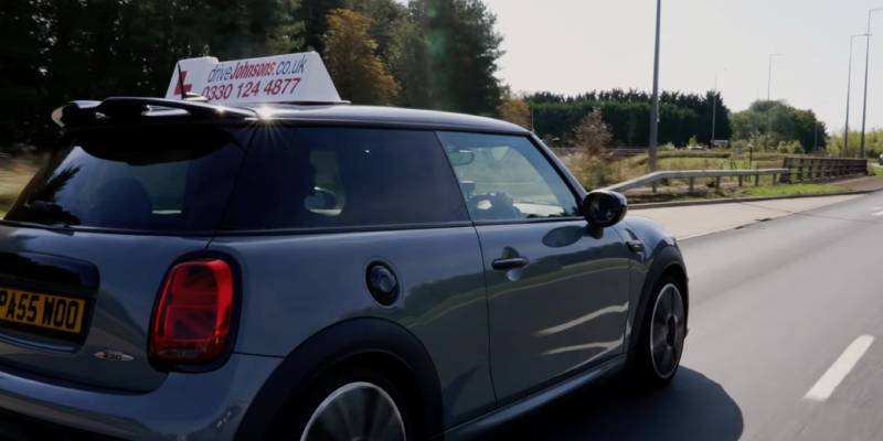 Mini Cooper with driveJohnson's roof sign on top driving on a dual carriageway