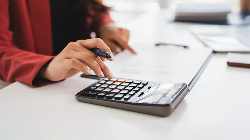 Hand pressing a calculator and pointing at paper