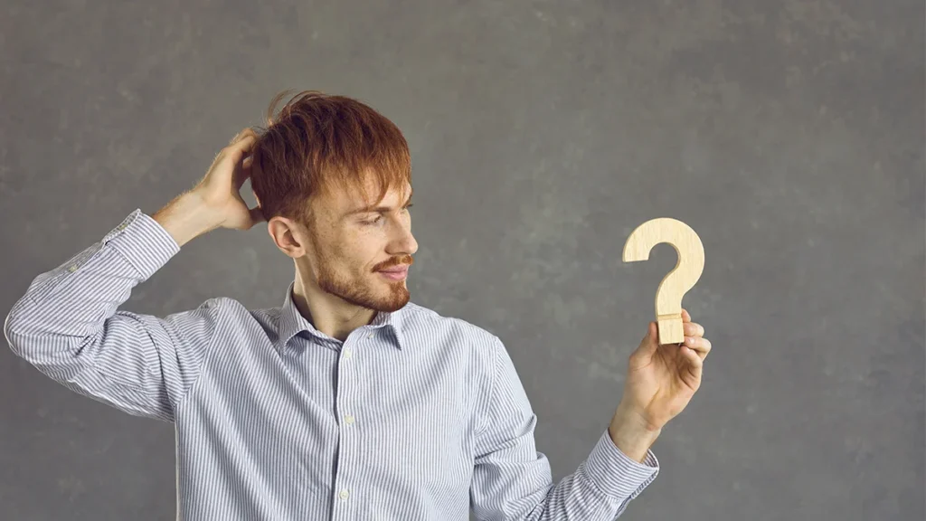 Man scratching his head and looking at question mark to symbolise being unsure